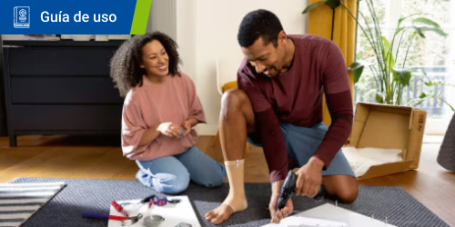 Un hombre con tobillera taladra un tablón de madera mientras una mujer le observa sonriente. Un hombre con tobillera taladra un tablón de madera mientras una mujer le observa sonriente.